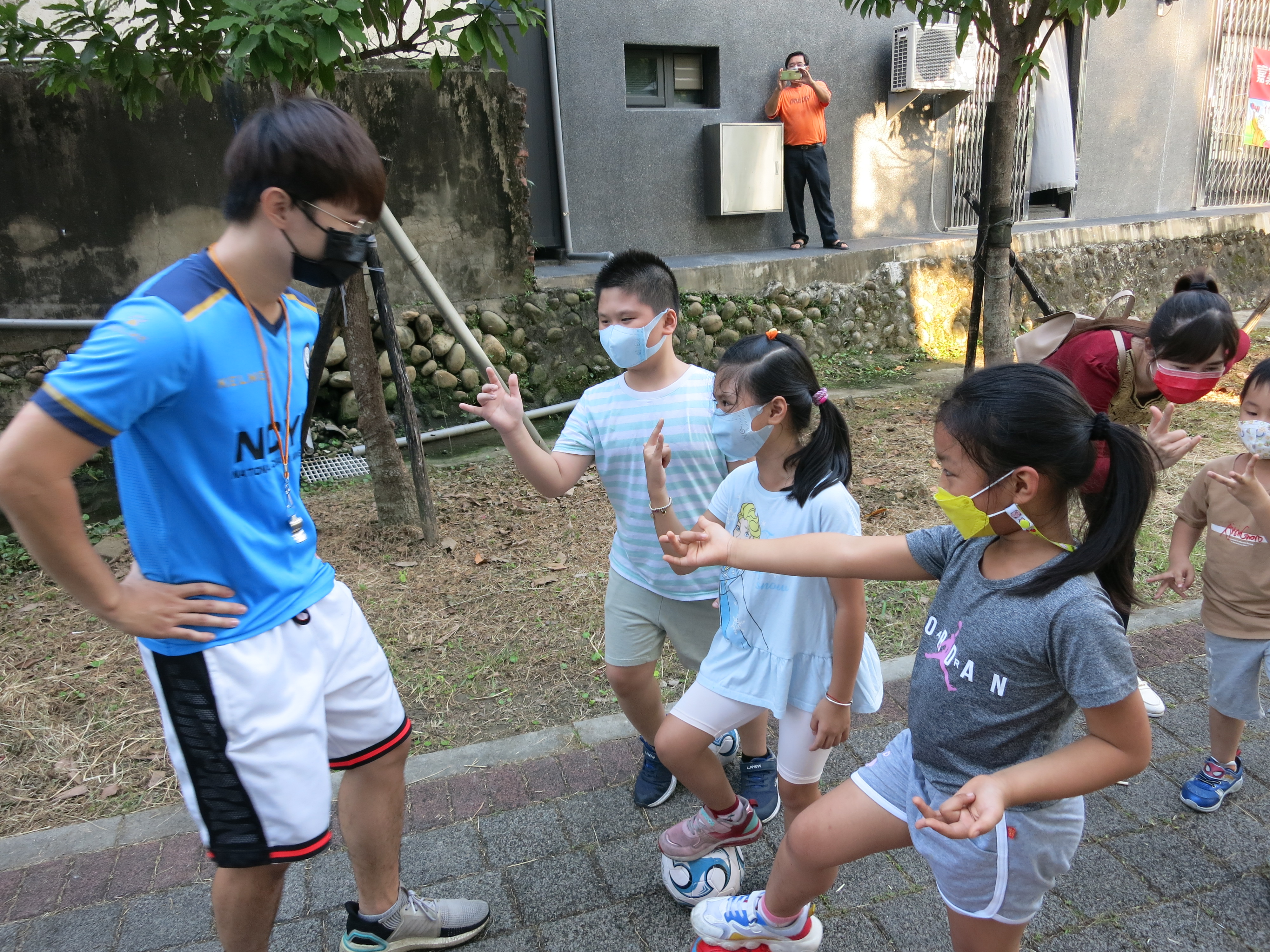 何誠晉香港新二代教導兒童一邊玩一二三木頭人，一邊練習控制足球。（圖／嘉義市服務站提供）