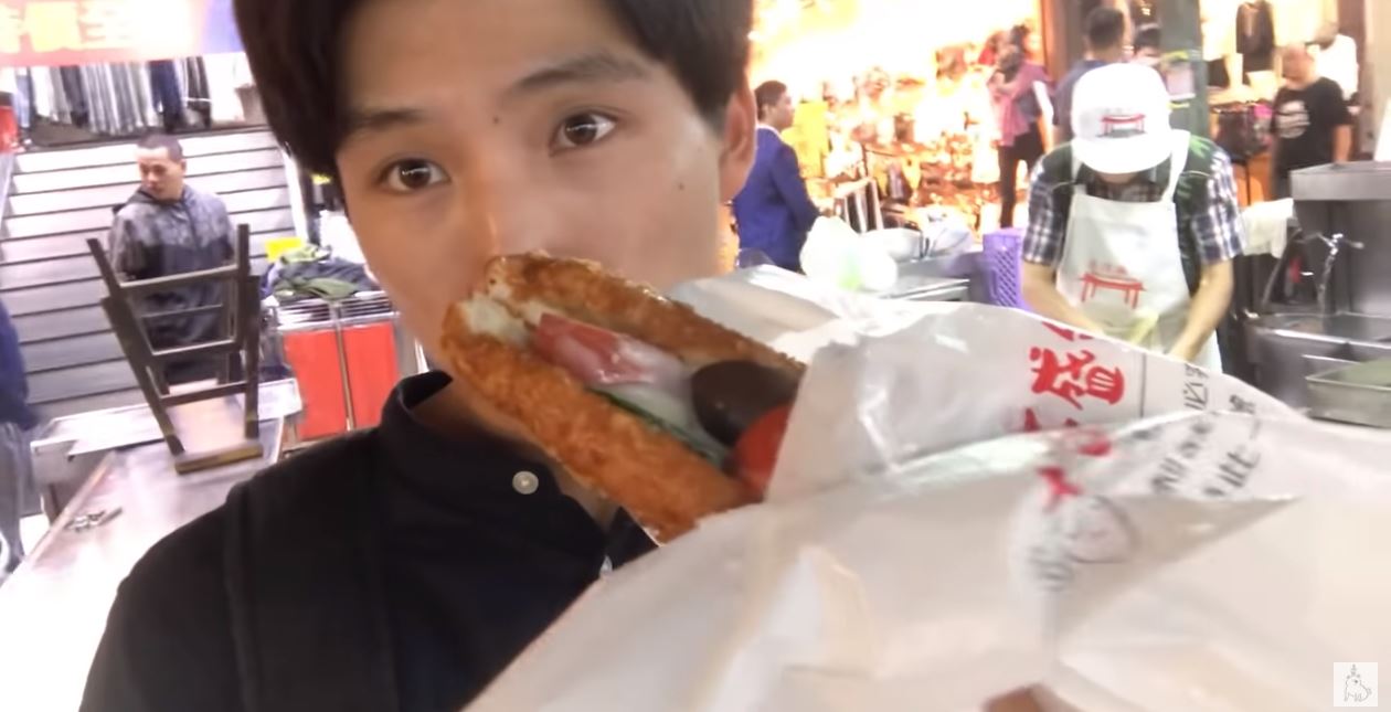 Suzuki katsunori thưởng thức bánh mì sandwich tại chợ đêm Miếu Khẩu – Cơ Long. (Nguồn ảnh: kênh YouTube 鈴木的日常 【台灣留學】)