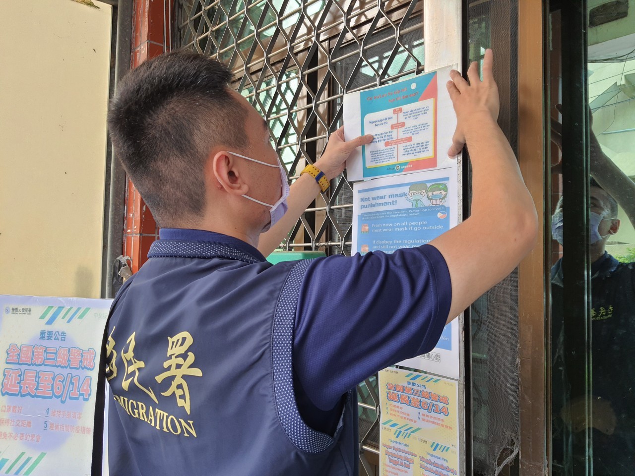 The National Immigration Agency Chiayi Country Brigade puts up a multi-lingual poster at the entrance of the migrant workers’ dormitory with the Covid-19 level 3 alert extension and other Covid-19 prevention measures. Photo/Provided by National Immigration Department Chiayi Service Station