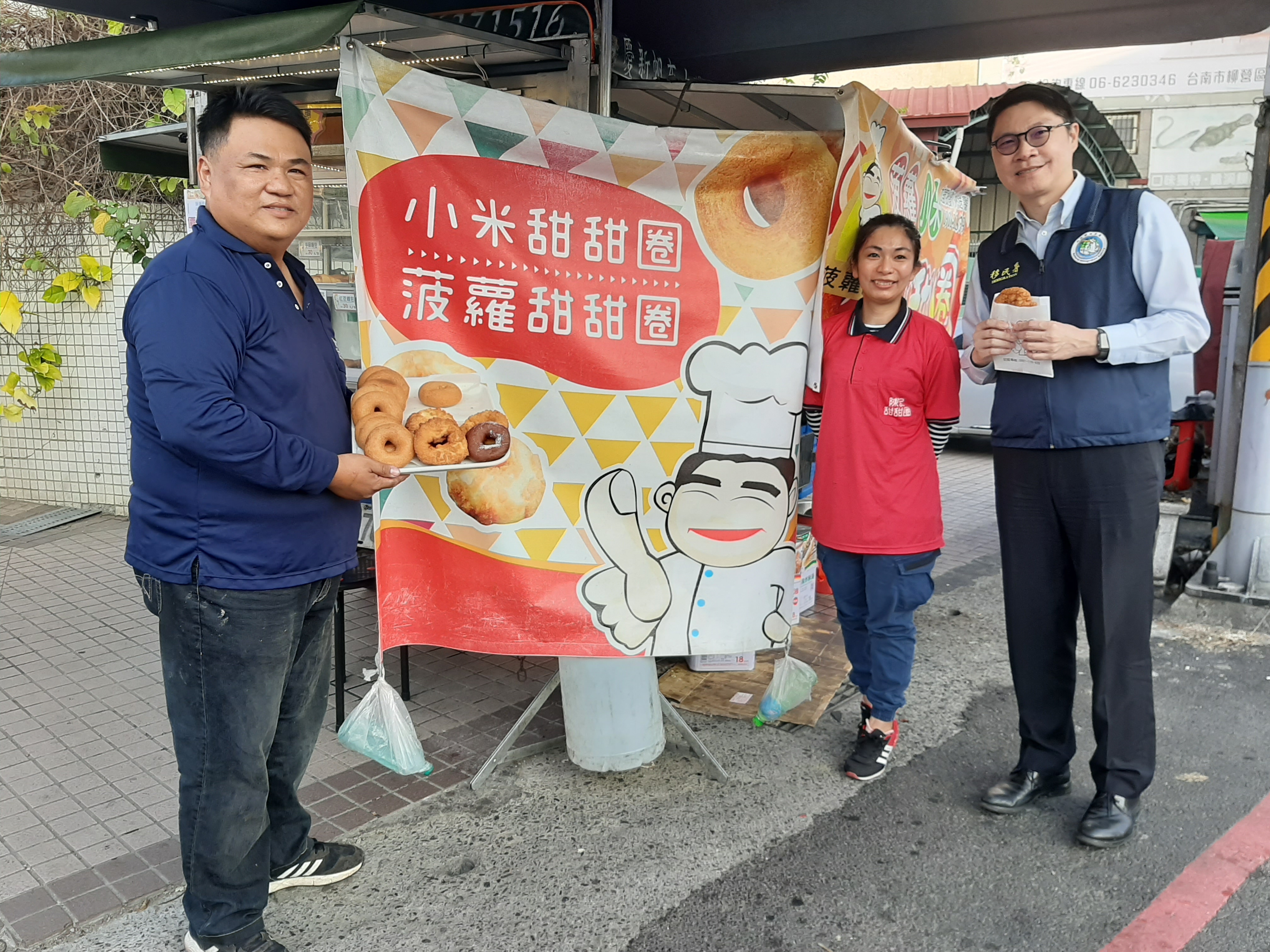 移民署臺南市第二服務站主任陳南翰(右一)前往新營探視越南新住民范鄭瑞綾(右二)和丈夫陳信達(左一)執行築夢計畫狀況，陳記甜甜圈商標是以瑞綾公公的卡通圖樣手比讚，代表傳承與對自家產品的自信(移民署臺南第二服務站提供)