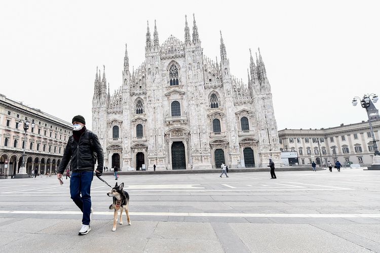 Seorang pria memakai masker berjalan dengan anjingnya di Duomo Square, Milan, Italia.(Sumber:Kompas)