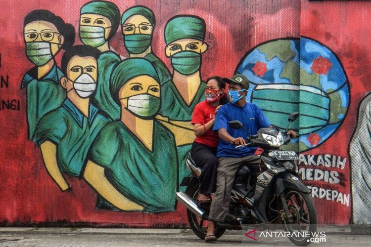 Pengendara motor melintas di depan mural tentang pandemi COVID-19 di Jalan Raya Jakarta-Bogor, Depok