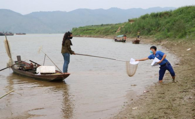 Một tình nguyện viên Đoàn xã Thanh Giang lội ra sông Lam phát bài tập cho các em làng chài.