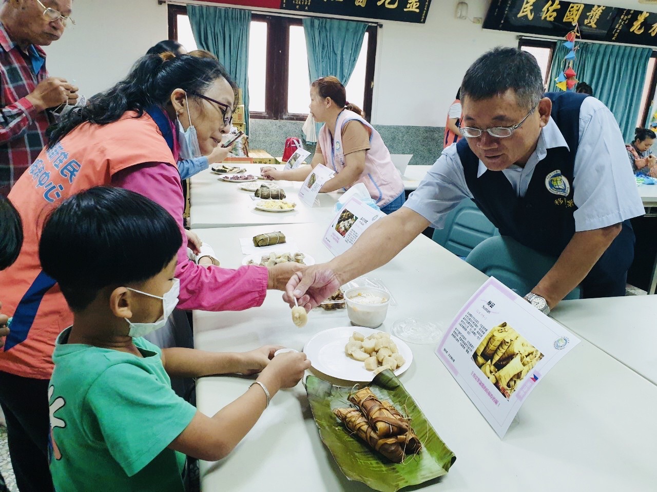 Nhân viên Trạm phục vụ Sở Di dân huyện Vân Lâm ông Wu Jing Xian cùng Cư dân mới thế hệ 2 ăn thử các loại bánh ú (ảnh: Trạm phục vụ Sở Di dân huyện Vân Lâm